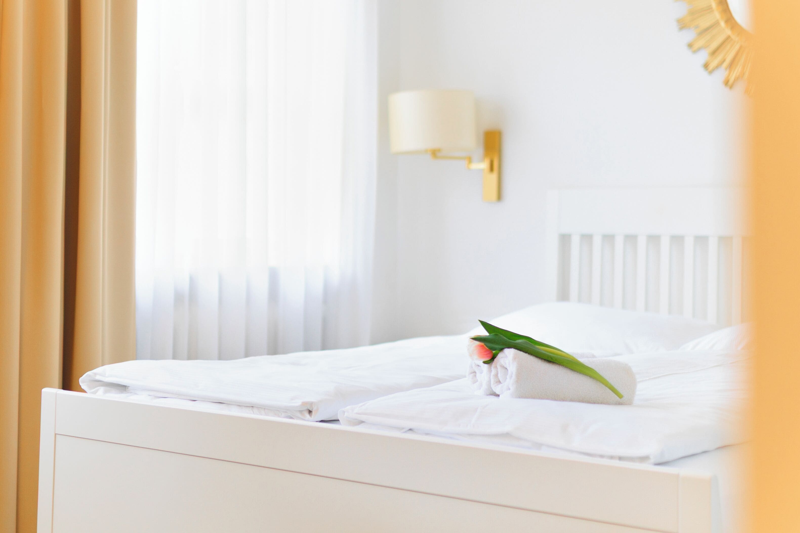 Ein Hotelzimmer mit einem ordentlich bezogenen Bett, einer Wandleuchte und einem Fenster mit Vorhängen.