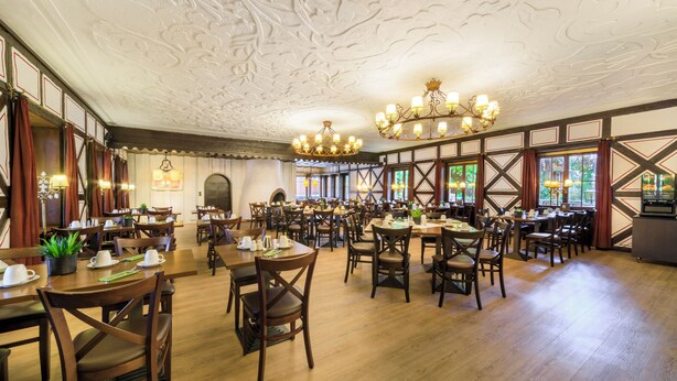 Une salle à manger spacieuse, avec des tables et des chaises en bois, un plafond décoré et de grandes fenêtres.