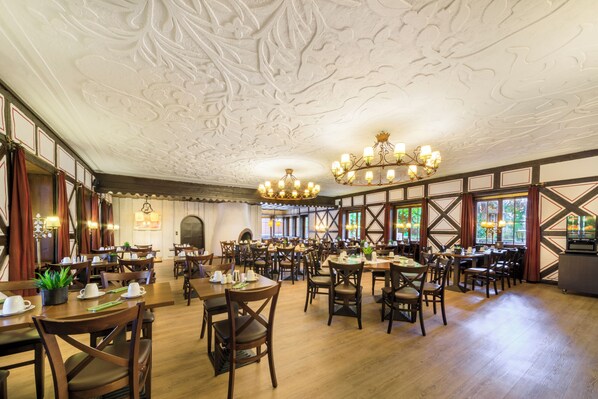 A spacious dining area with wooden tables and chairs, ornate ceiling, and large windows. - relexa Waldhotel Schatten (Stuttgart)