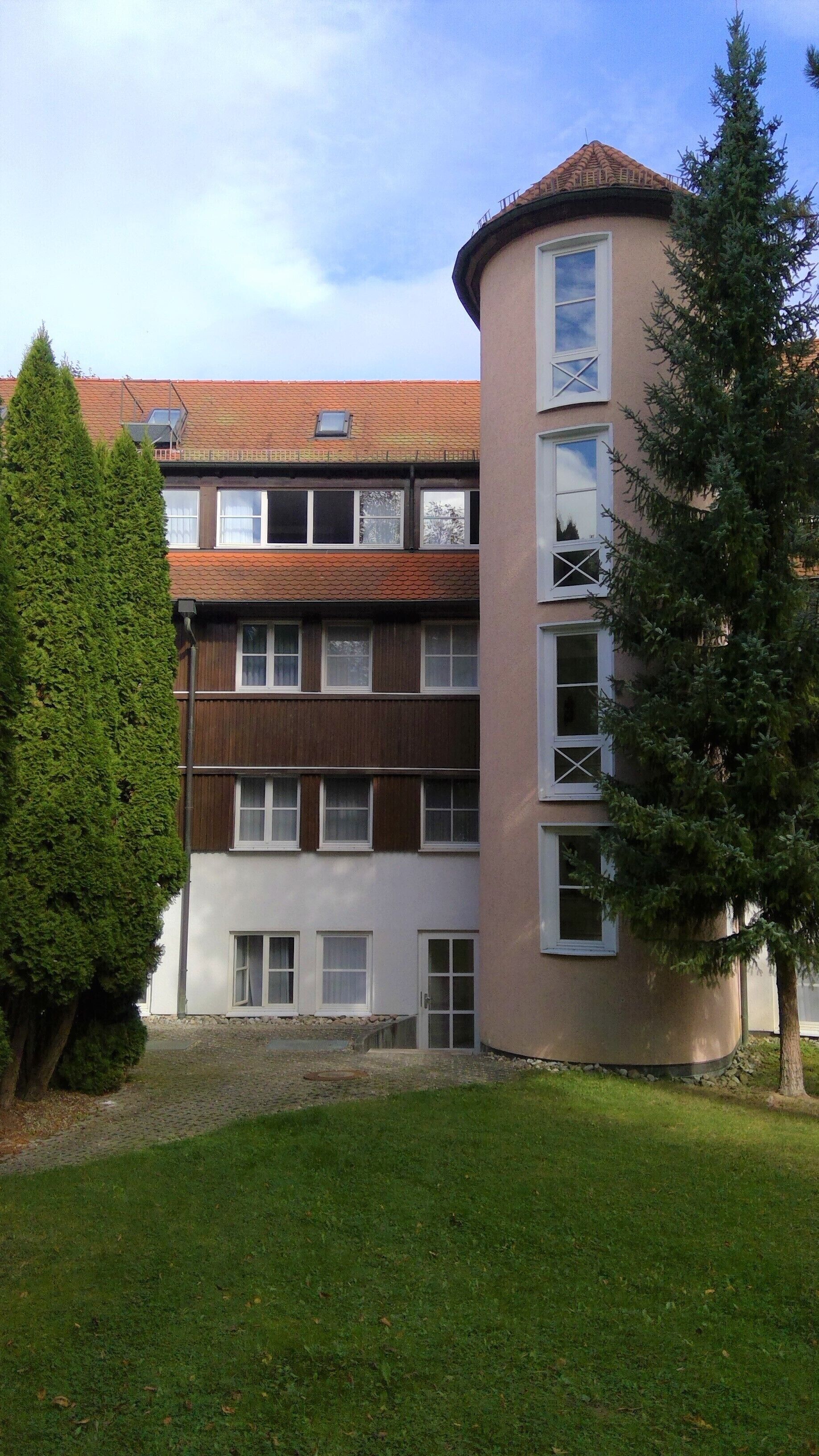 Un edificio de varios pisos con fachadas de madera y enlucido, un techo de tejas y un pequeño balcón.