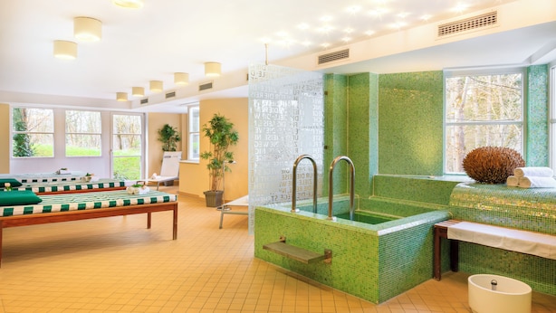 Une salle de spa avec un mur recouvert d’une mosaïque verte, un jacuzzi et une table de massage.