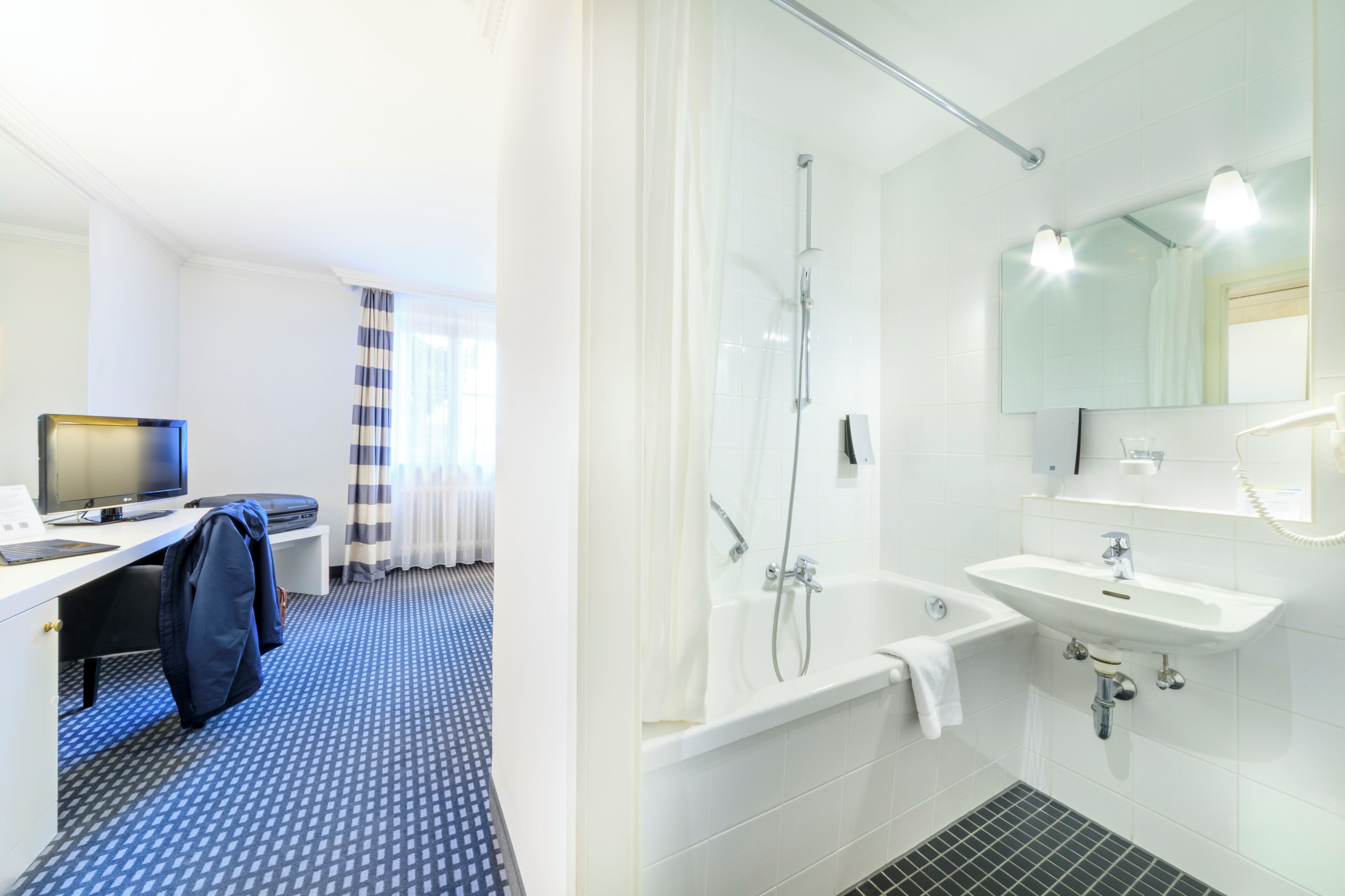 Habitación de hotel con escritorio, computadora y zona de ducha.