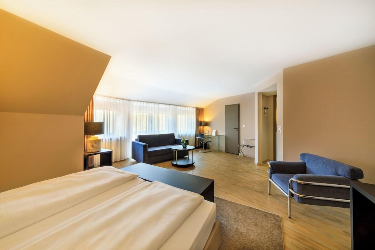 A hotel room with a large bed, a sofa, a desk, and a chair.