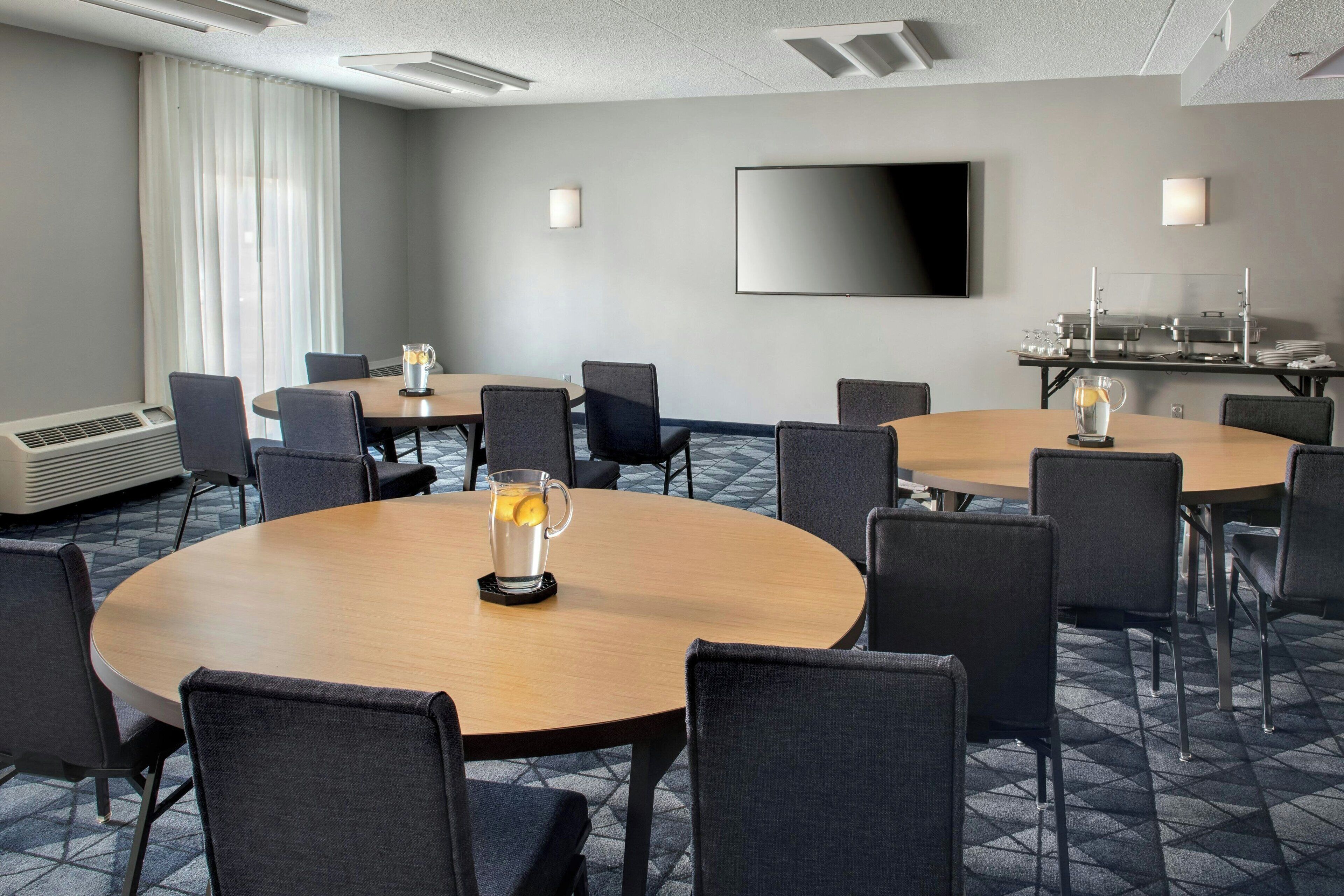 Un salón de conferencias con mesas redondas, sillas, un televisor de pantalla plana y una mesa de buffet.