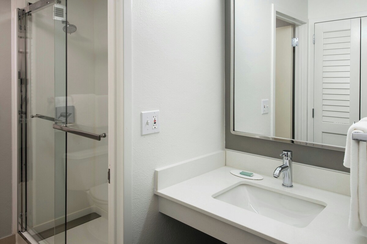 A modern bathroom with a glass shower enclosure, a white sink with a mirror above it, and a towel hanging on the wall.