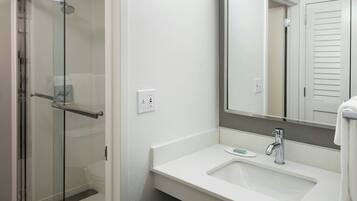 A modern bathroom with a glass shower enclosure, a white sink with a mirror above it, and a towel hanging on the wall.