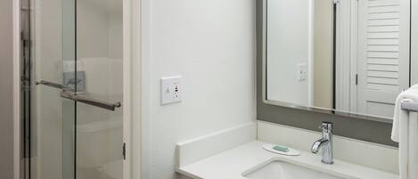 Ein modernes Badezimmer mit Duschkabine aus Glas, einem weißen Waschbecken mit Spiegel darüber und einem Handtuch an der Wand.