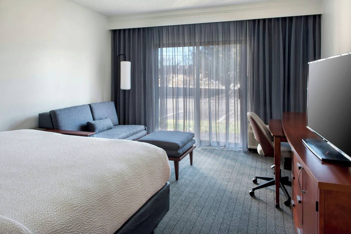 Habitación de hotel con una cama grande, un escritorio, una silla, un sofá y vistas al exterior a través de la ventana.
