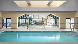 An indoor swimming pool with clear glass walls, lounge chairs, and a view of the outside. - Courtyard by Marriott Annapolis (Annapolis)