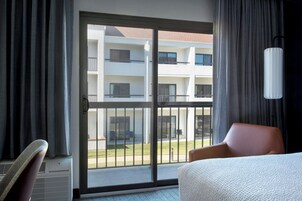 Habitación de hotel con cama, una silla, una ventana y cortina, con vista a un edificio.