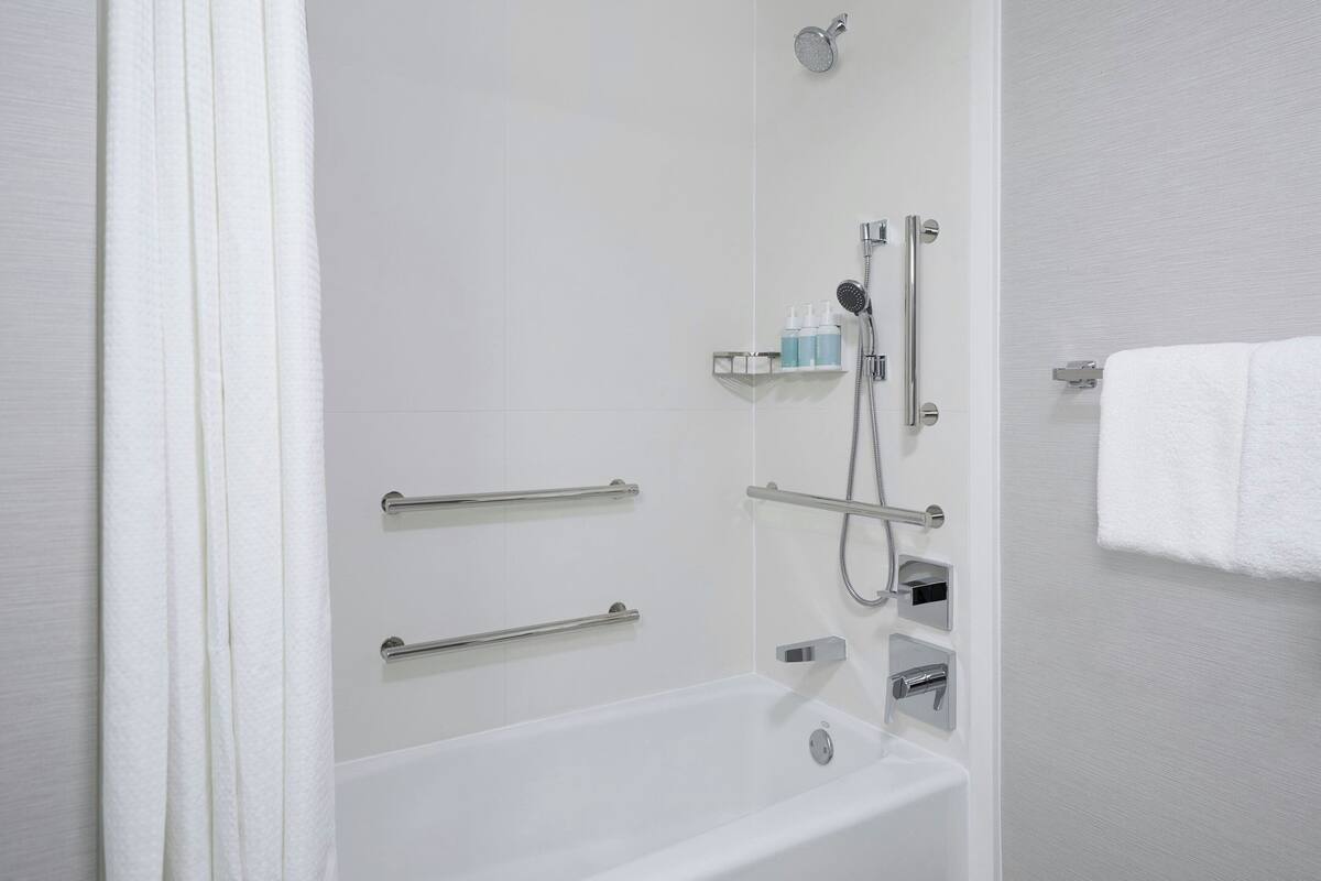 Ein modernes Badezimmer mit Badewanne, Dusche und Haltegriffen.