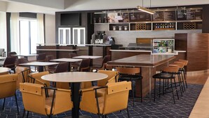 Un moderno vestíbulo de hotel con mesas y sillas redondas, una zona de bar y una máquina de café.