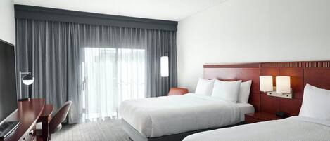 A hotel room with two beds, a desk, a chair, and a TV.