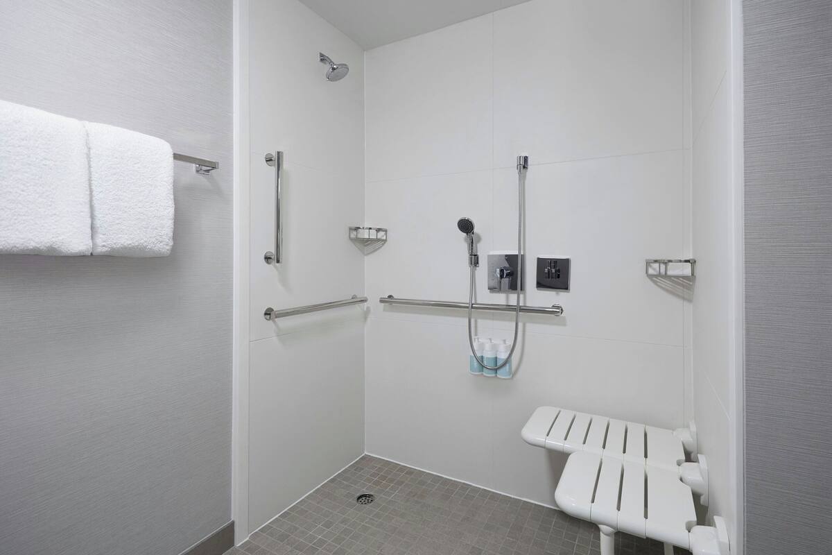 Ein modernes Badezimmer mit Dusche, Haltegriffen, einem WC mit Sicherheitsstütze und einem Handtuchhalter.
