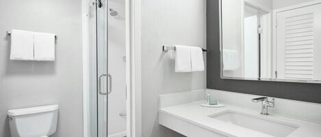 Un baño moderno con ducha de vidrio, lavamanos blanco y un espejo grande.