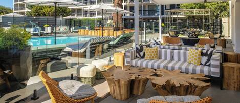 An outdoor lounge area with a pool, wicker furniture, and a modern building in the background.