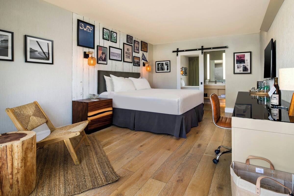 A bedroom with a bed, a desk, a chair, a wooden floor, and wall-mounted pictures.