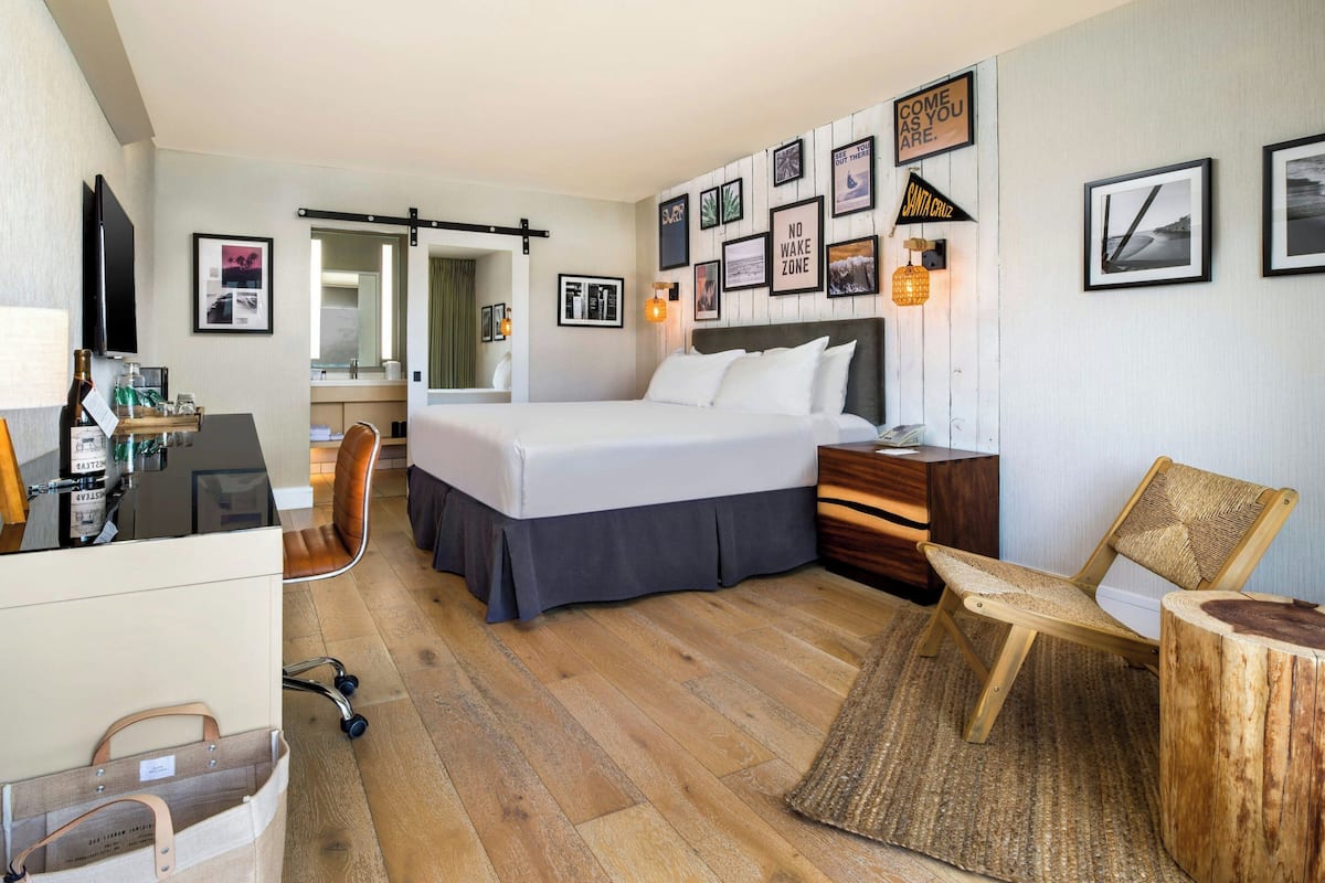 A hotel room with a bed, a desk, a chair, a mirror, and wall-mounted pictures.