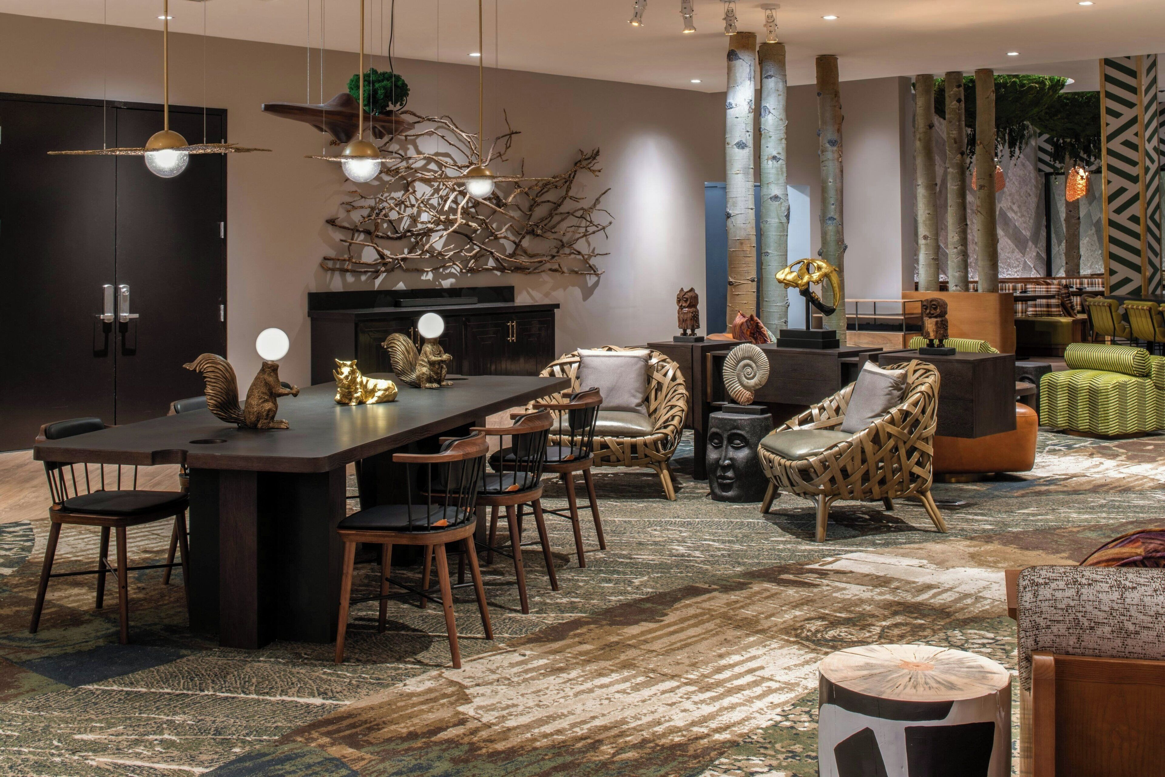 A modern living room with a dark wood dining table, comfortable seating, and a large tree sculpture.