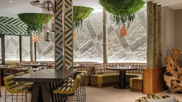 A modern interior with a large dining table, multiple seating areas, and hanging green foliage decorations.
