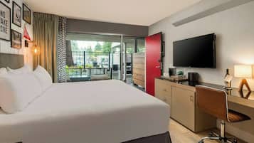 Habitación de hotel con cama, escritorio, televisor y balcón con mobiliario exterior.