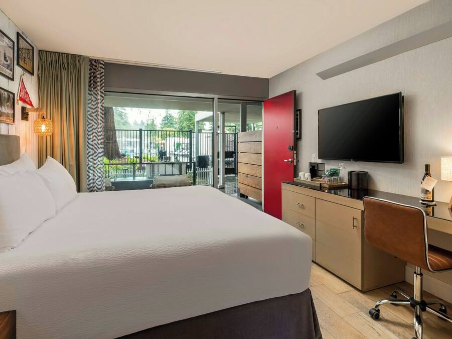 Habitación de hotel con cama, escritorio, televisor y balcón con mobiliario exterior.