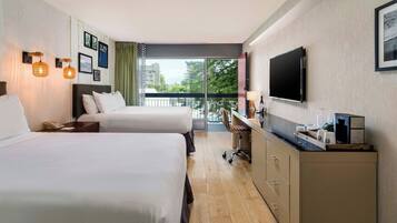 Ein Hotelzimmer mit zwei Betten, einem Schreibtisch, einem Fernseher und einem Balkon mit Blick.