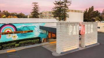 Entrada de un hotel con un mural de olas y flores, un letrero que dice "PARADOX" y un edificio moderno al fondo.