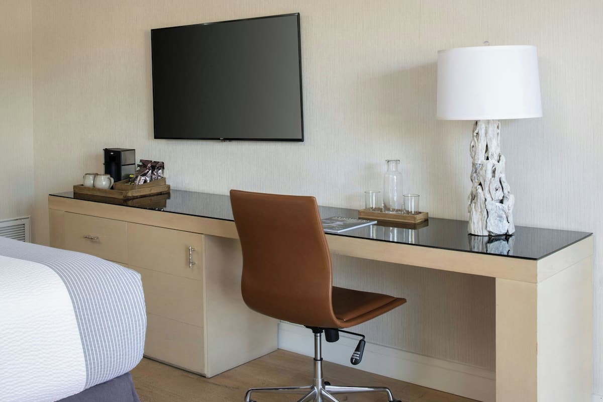 A hotel room with a bed, a desk with a chair, a flat-screen TV, a lamp, and a coffee maker.