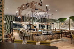 Un área de bar moderna con mostrador de mármol, luces colgantes y paredes con diseño verde.