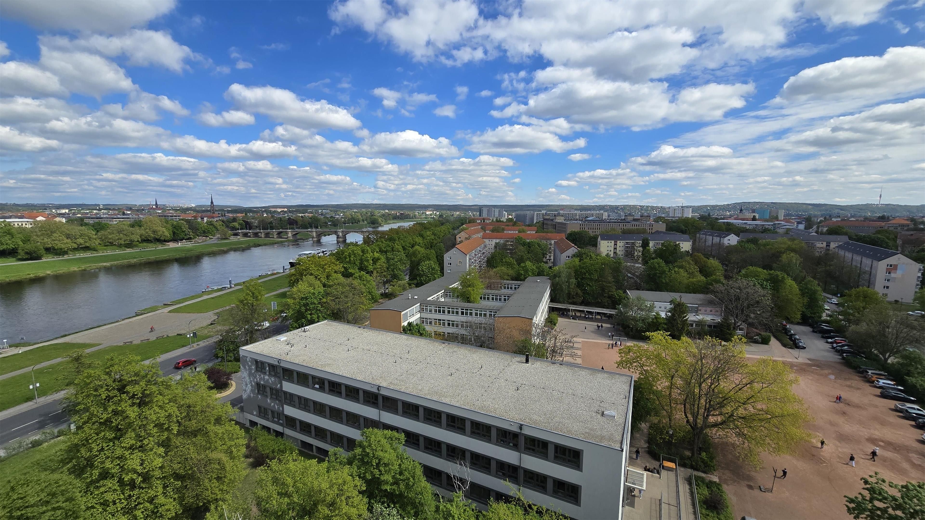 A riverside view of a campus with buildings, a bridge, and a clear sky.