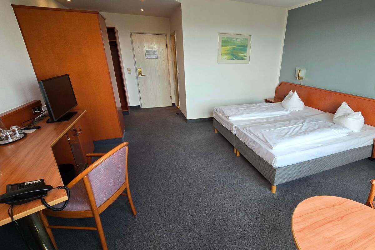 A hotel room with a bed, desk, chair, and a small table.