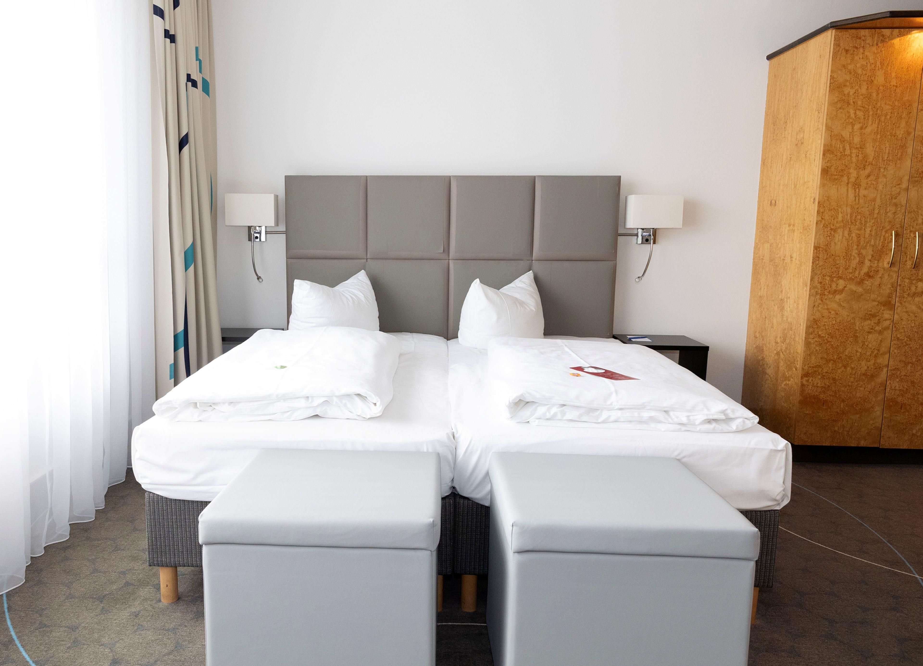 Een tweepersoonsbed met een grijs hoofdeinde, twee nachtkastjes en een houten garderobe.