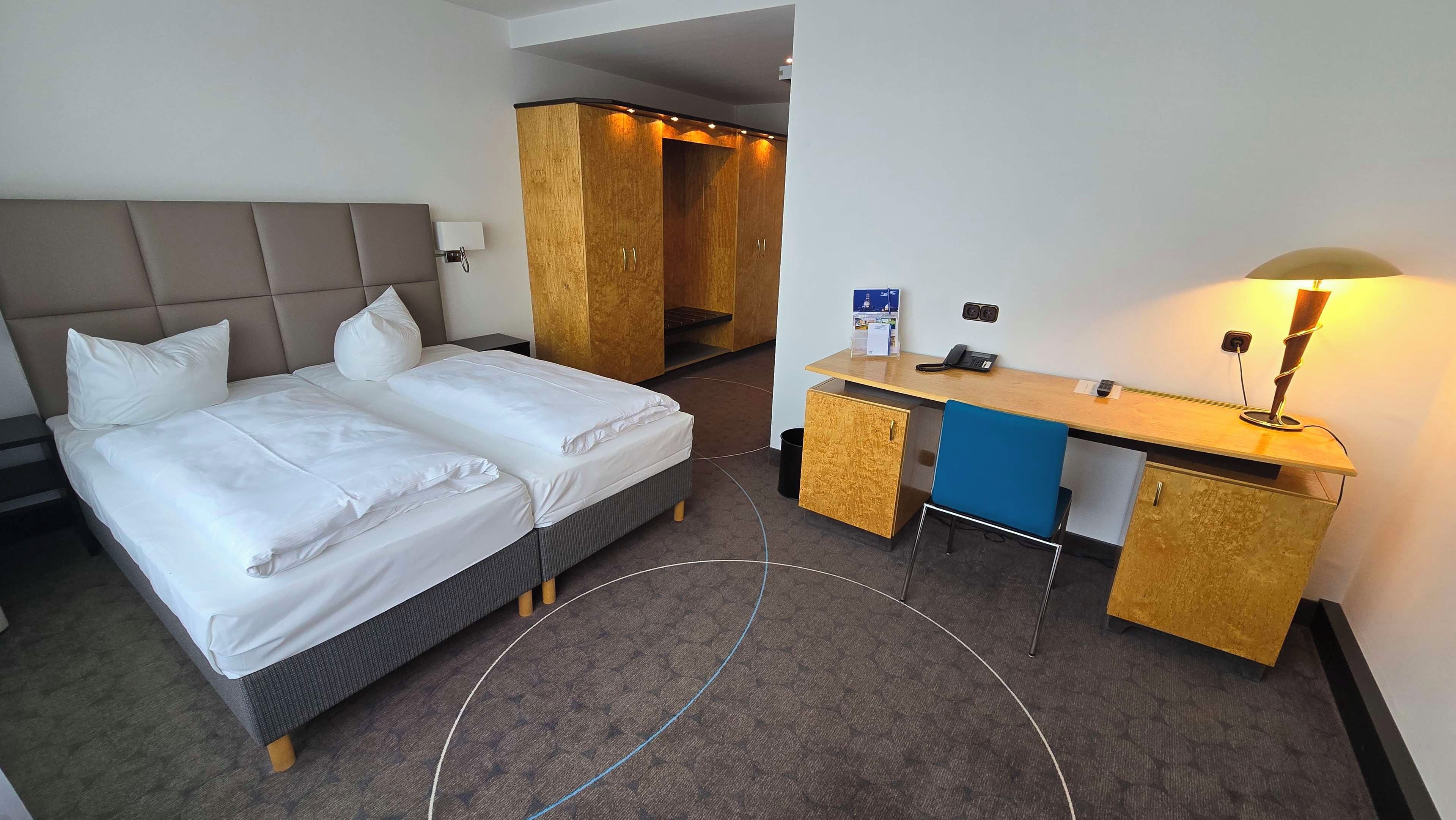 Hotellihuone, jossa on sänky, työpöytä, lamppu ja vaatekaappi.