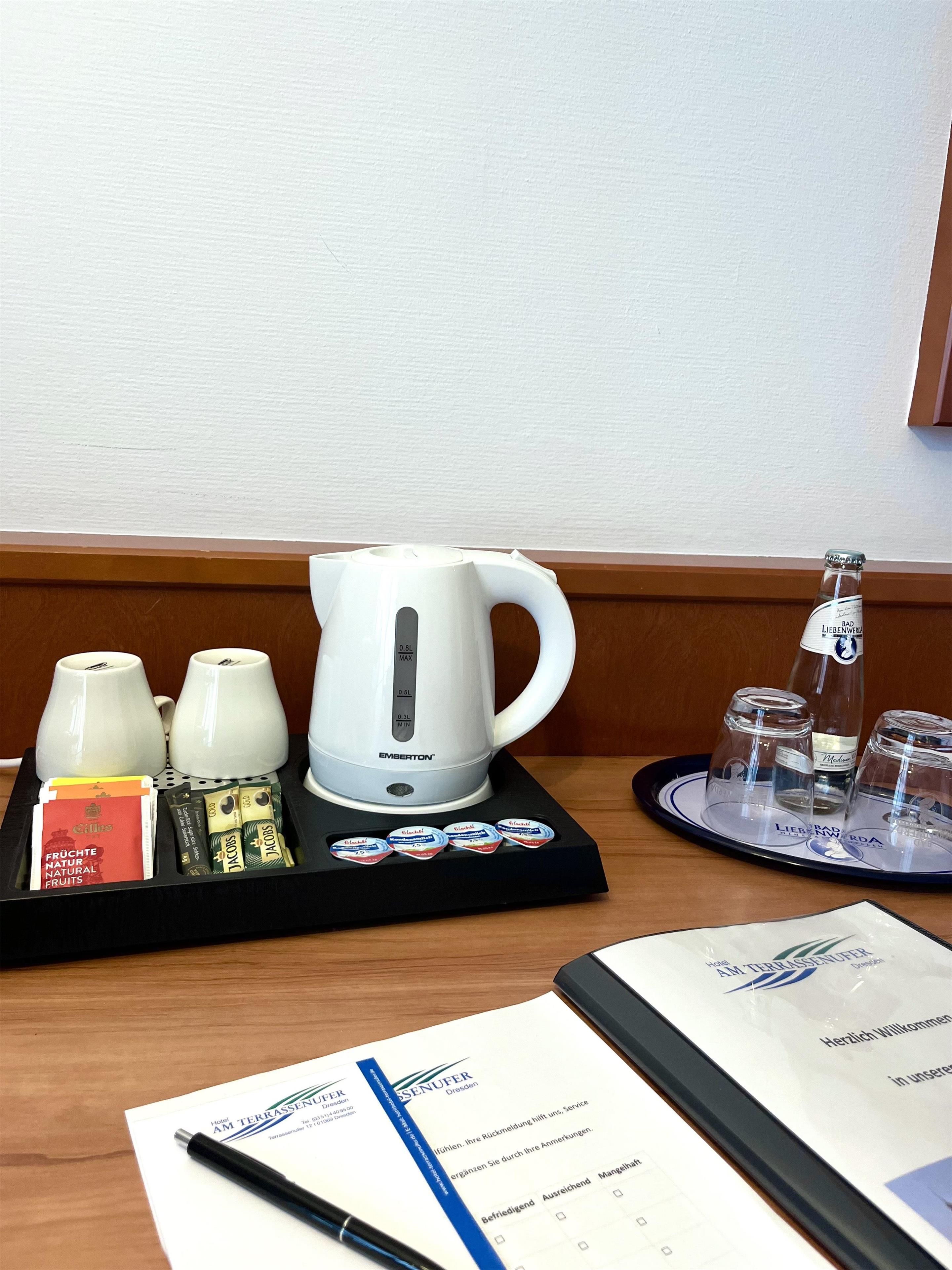 A hotel room with a tray of tea bags, a kettle, and glasses on a tray.