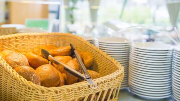 A wicker basket filled with bread rolls and a pair of tongs, alongside stacked white plates.
