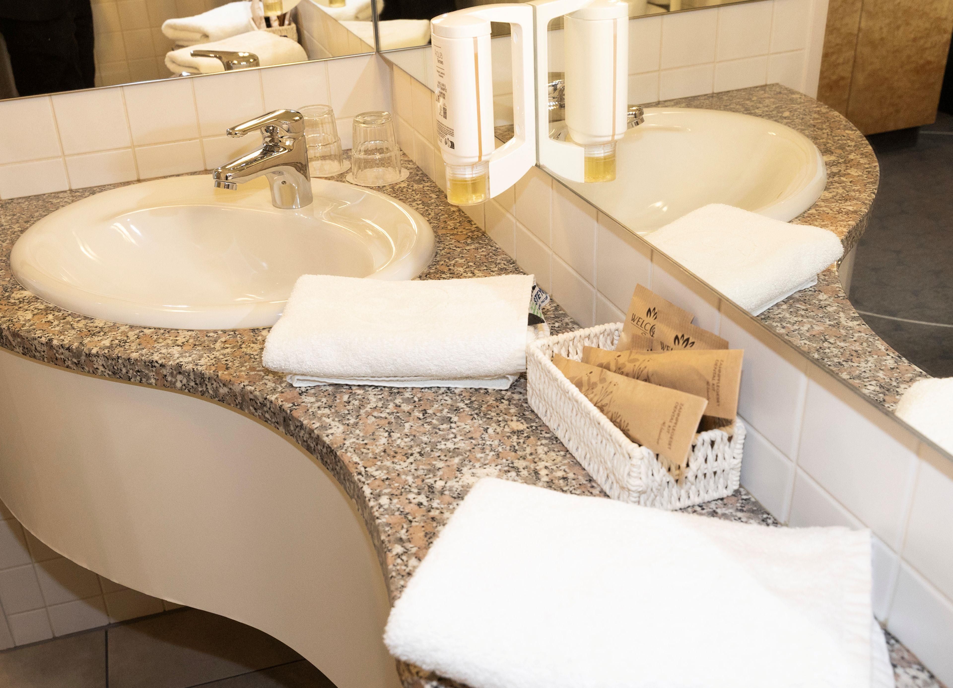 A bathroom with two sinks, a mirror, and a basket of toiletries.