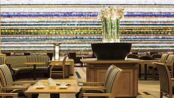 A restaurant with striped chairs and tables, a large black vase with flowers, and a colorful mosaic wall in the background.