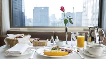 A breakfast table with a city view, including a rose, a pitcher, and a plate of food.