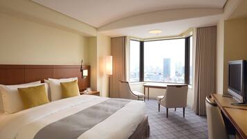 Een hotelkamer met een groot bed, een bureau, een stoel, een televisie en uitzicht op de stad.