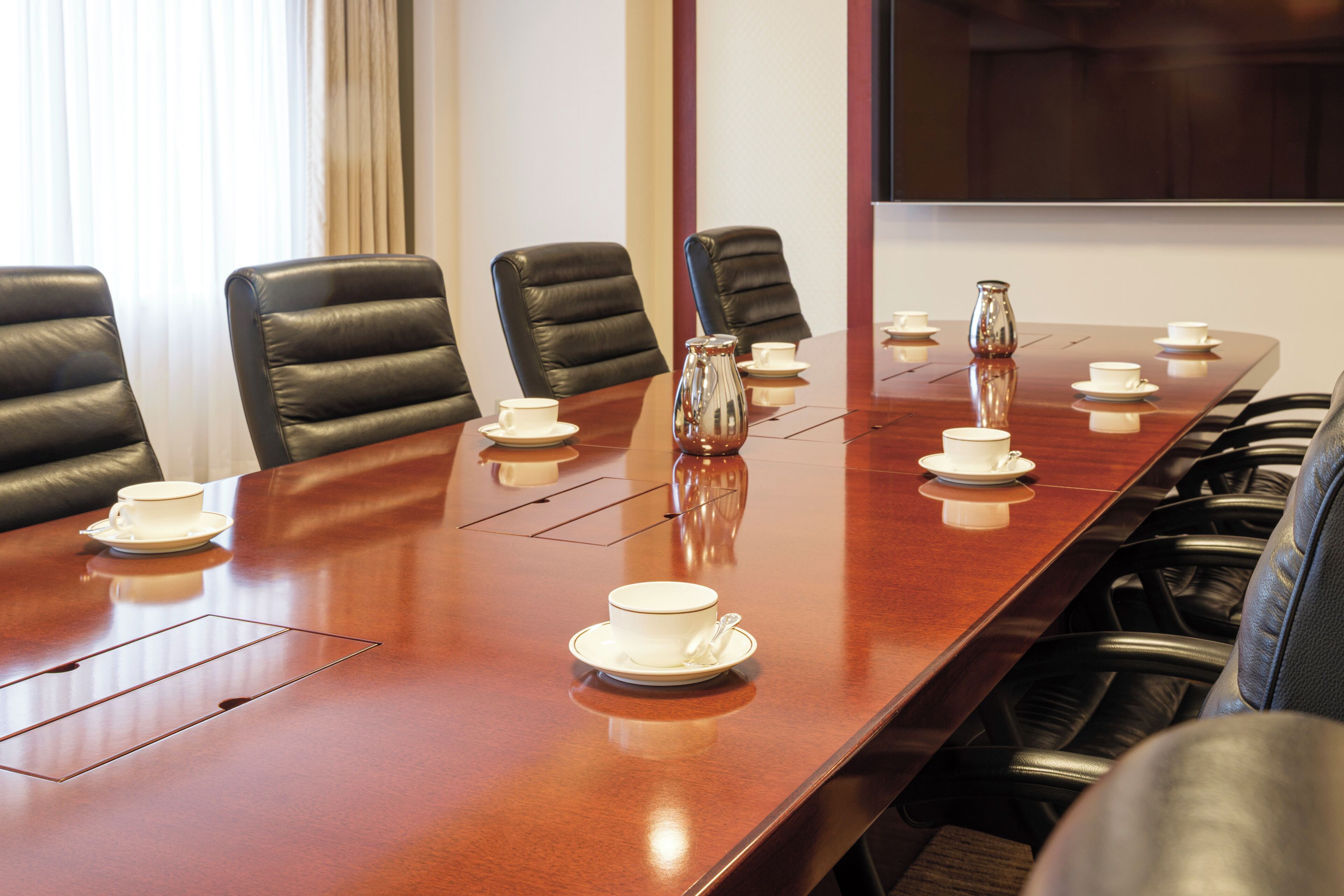 A conference room with a long table, multiple chairs, and several white cups and saucers.
