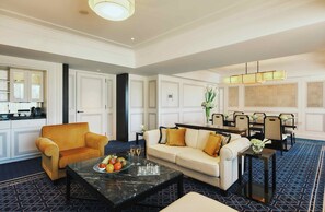 A spacious living area with a sofa, armchair, and a coffee table. There is a dining area with chairs and a chandelier.