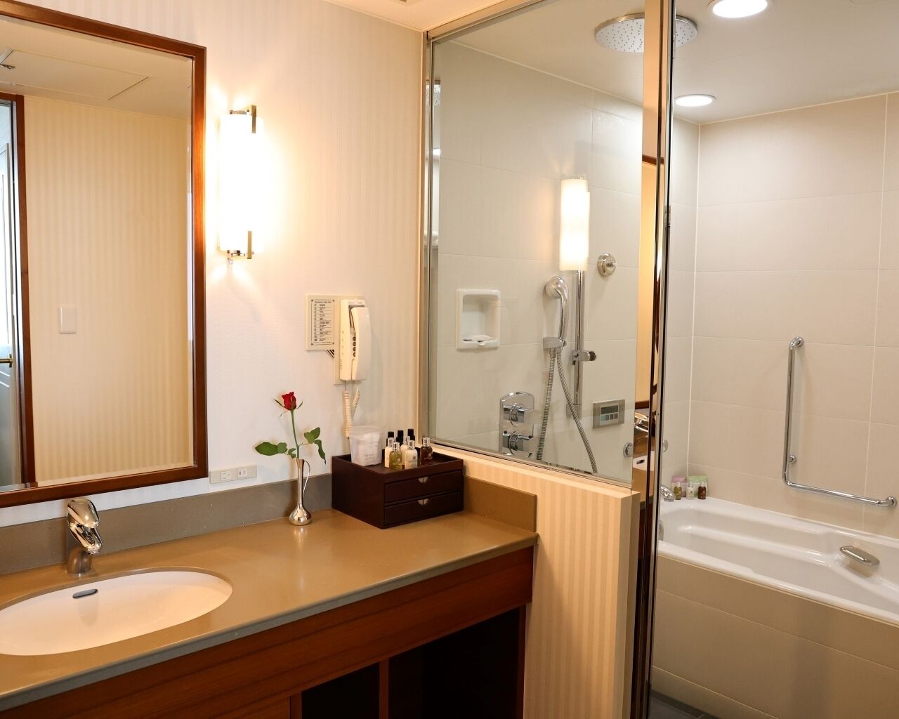 A hotel bathroom with a sink, mirror, vanity, shower, and bathtub.