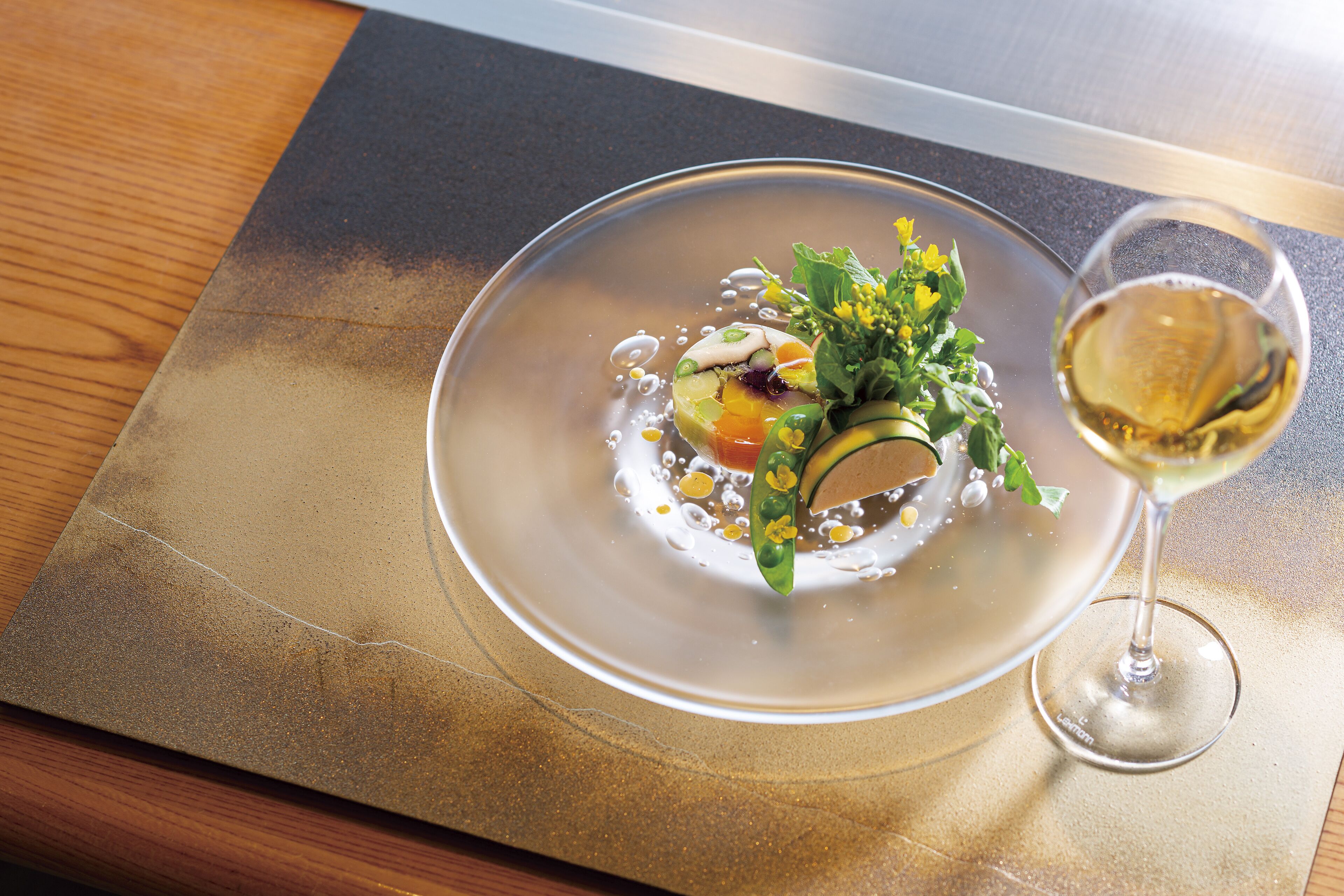 A plate of food with a glass of white wine on a table.