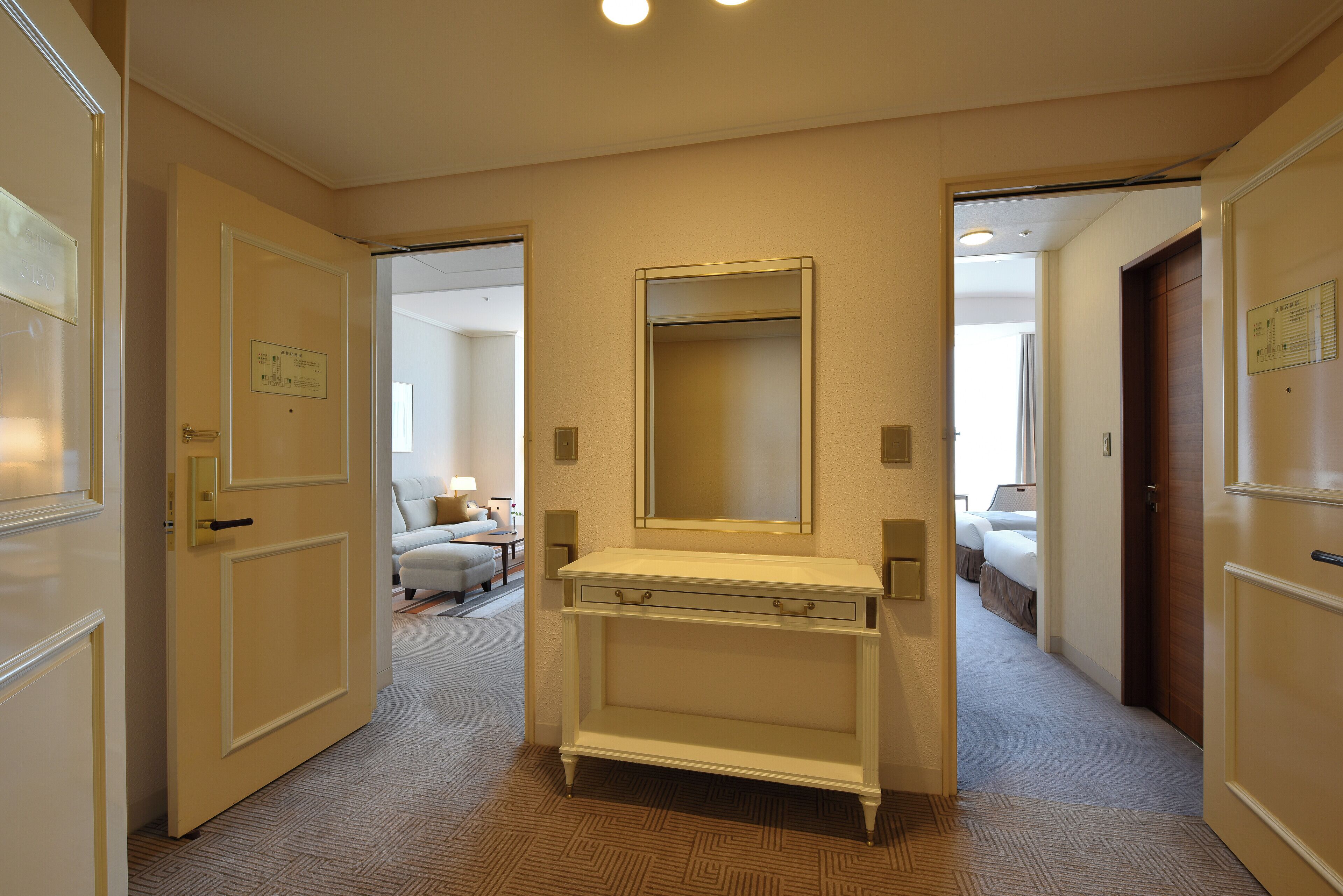 A hotel hallway with a white console table, a large mirror, and a door leading to a bedroom.
