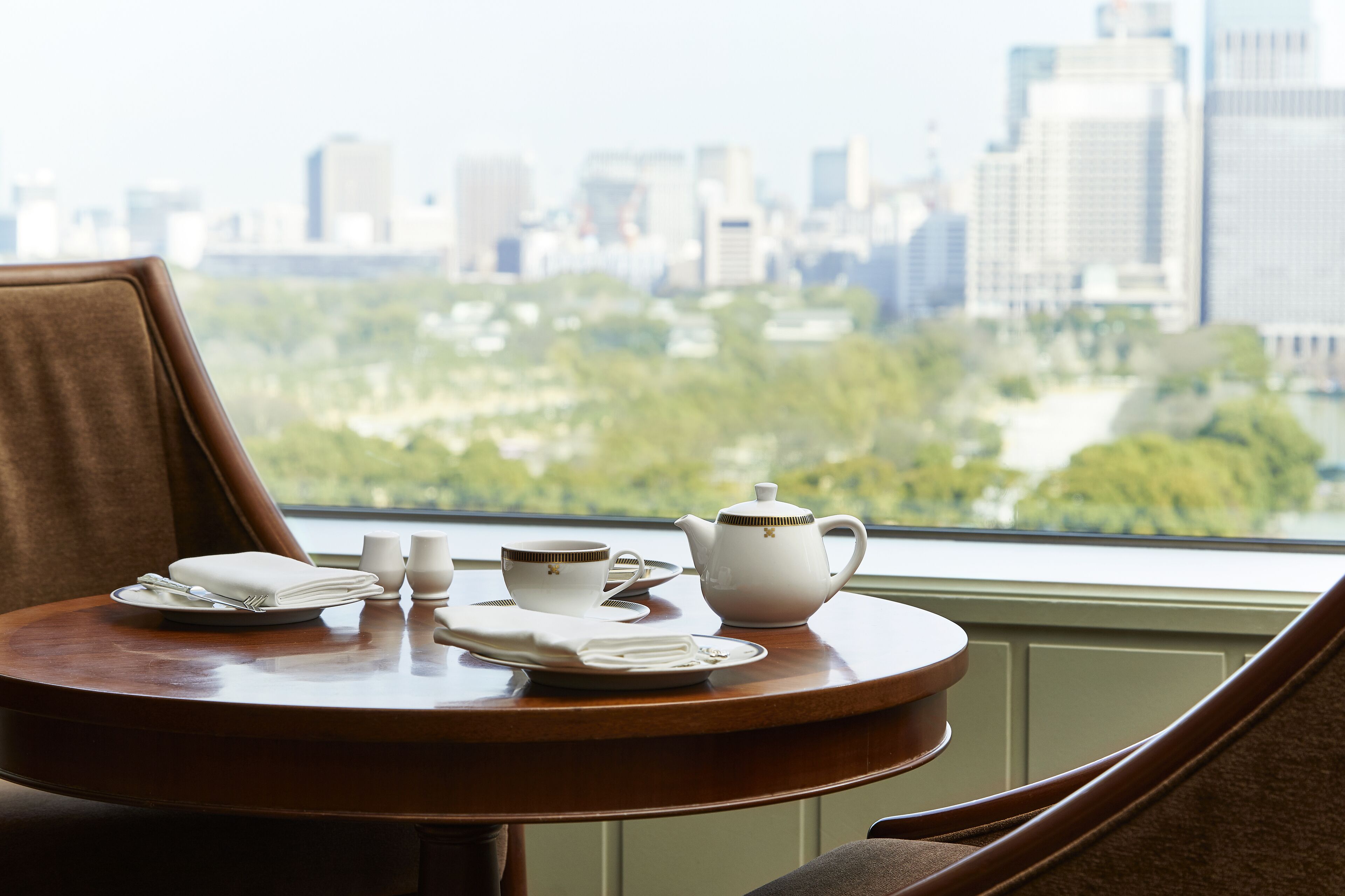 A dining table with a tea set and a view of a cityscape through a window.