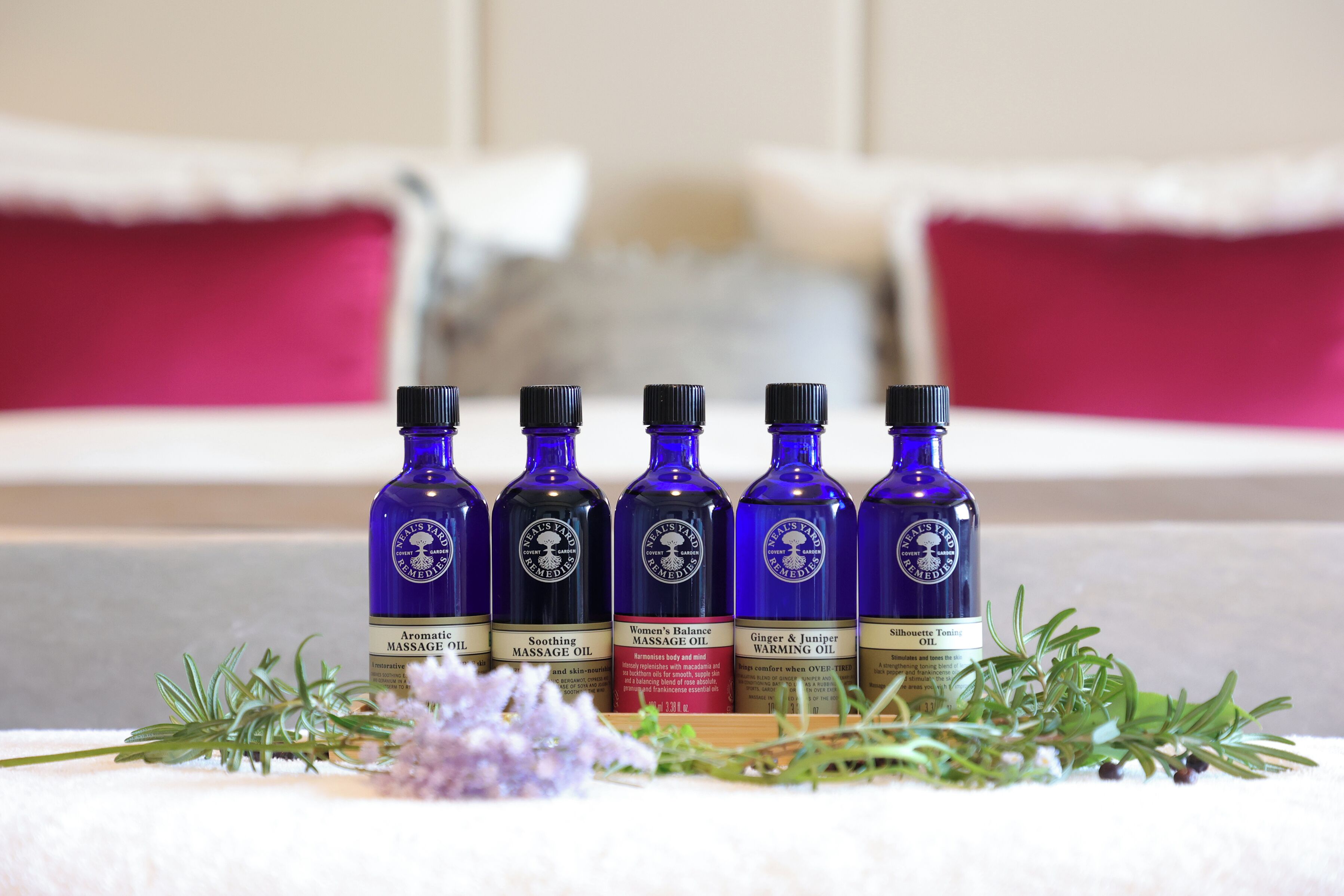 Five bottles of massage oil on a table with a white towel and some herbs.