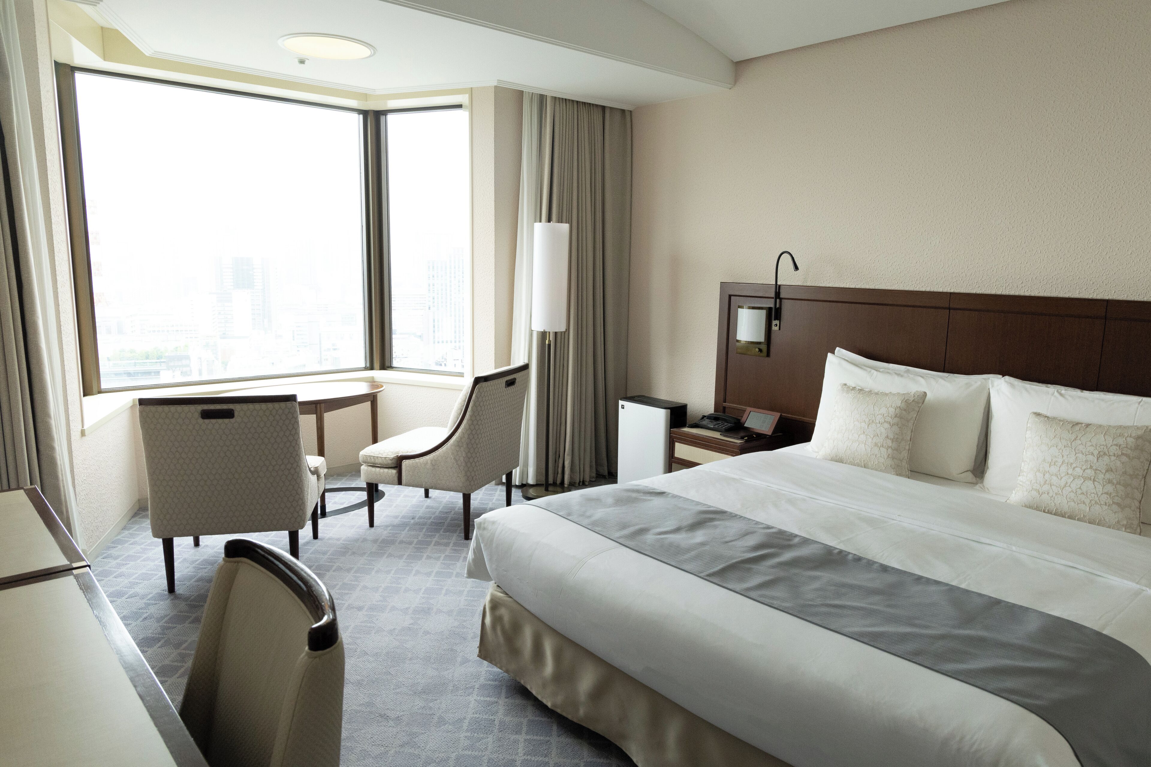 A hotel room with a large bed, a desk, a chair, and a view of the city.