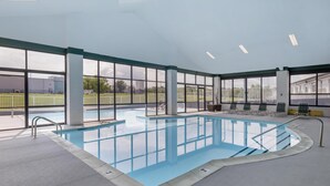 En inomhuspool med väggar av genomskinligt glas, ett kaklat golv och några solstolar.