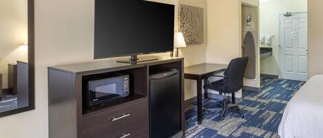 Une chambre d’hôtel équipée d’une télévision à écran plat, d’un four à micro-ondes, d’un réfrigérateur, d’un bureau avec une chaise et d’un lit.